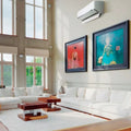 Moderne luft-til-luft varmepumpe monteret i lys stue med hvide møbler og store vinduespartier.
